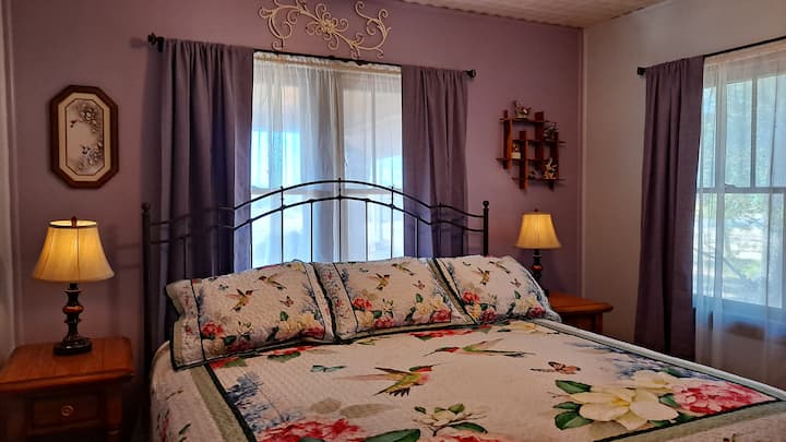 Bedroom 1 -- Master bedroom. The Hummingbird Room with king-size bed and private bathroom. Darkening curtains. USB charging ports in lamp bases. Ceiling fan.