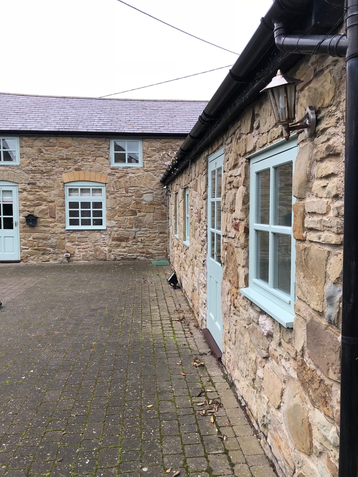 A stone-clad exterior displays a pathway bordered by carefully arranged cobblestones. Light blue window frames accentuate the rustic charm of the building, while a vintage lantern adds to the inviting ambiance of the entrance.