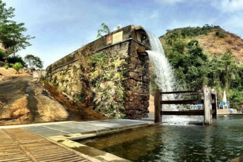 Lateral da piscina natural com cachoeira e área de deck exclusiva para hóspedes.