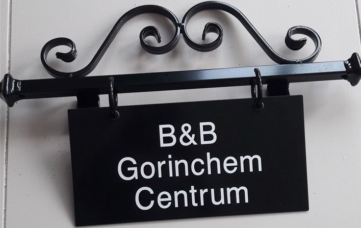 A black metal sign is displayed, featuring the text 'B&B Gorinchem Centrum' in white lettering. The sign is hung from an ornate, scroll-patterned bracket, contributing to the establishment's overall character.