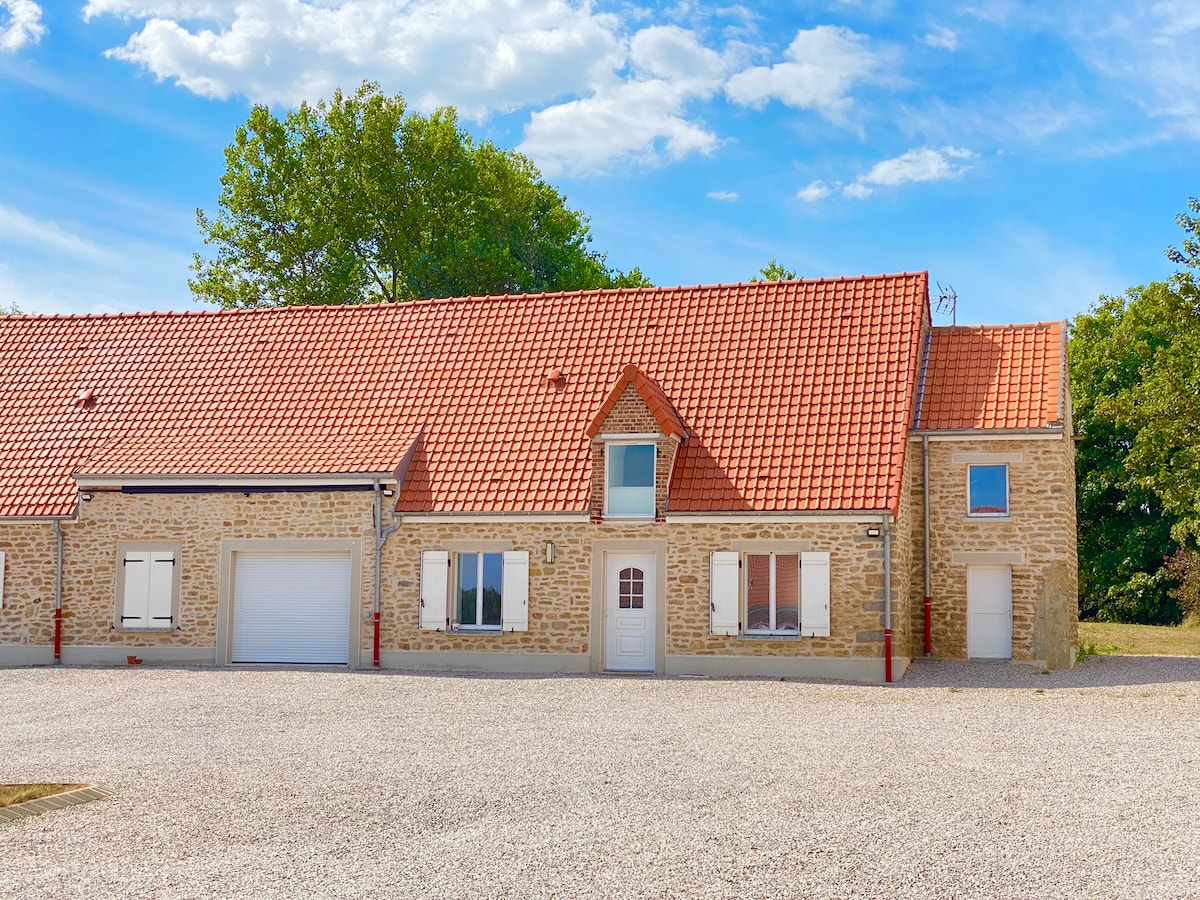 The exterior of a renovated stone house is highlighted, featuring a red tiled roof and white window shutters. A gravel driveway leads to the front door, framed by greenery. The structure showcases a mix of rustic charm and modern design elements.