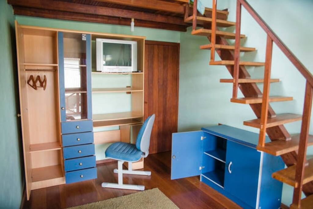 Escadaria que sobe para o mezanino, guarda roupas com escrivaninha e balcão para guardar sua bagagem.