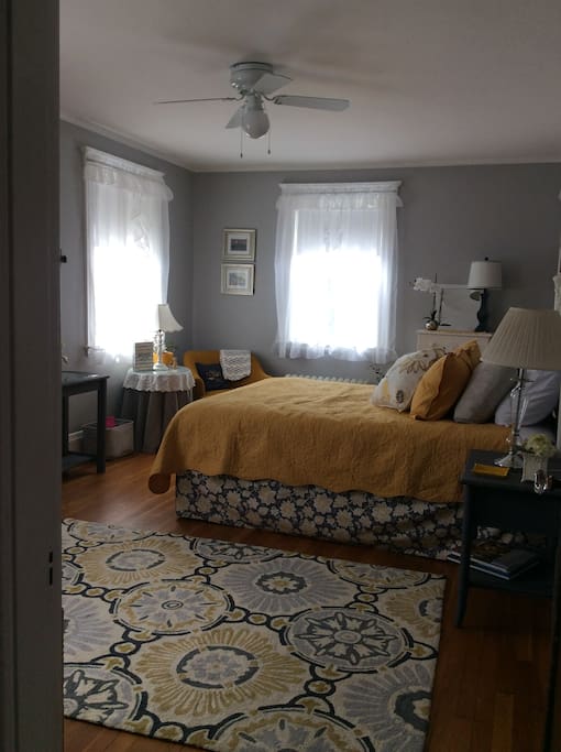 "The Grey Room" is a private room with a queen bed, TV, table, and fan.