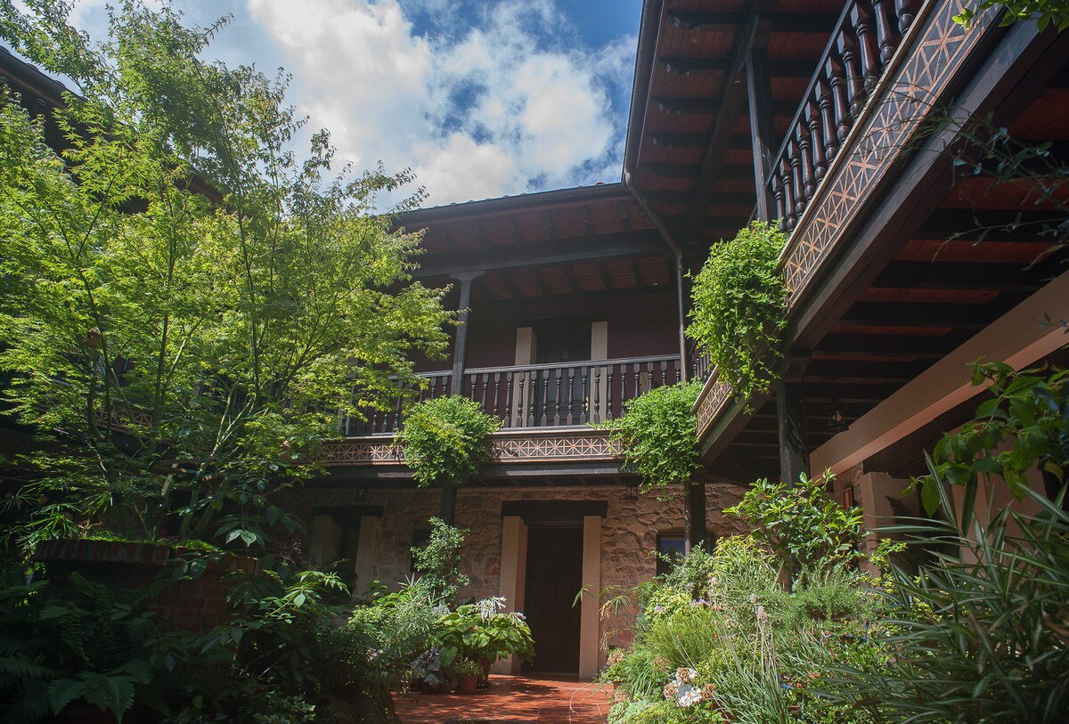 An interior courtyard is surrounded by multiple levels of balconies, featuring wooden beams and decorative railings. Lush greenery and vibrant plants add natural beauty, creating a serene environment that sets the tone for relaxation.