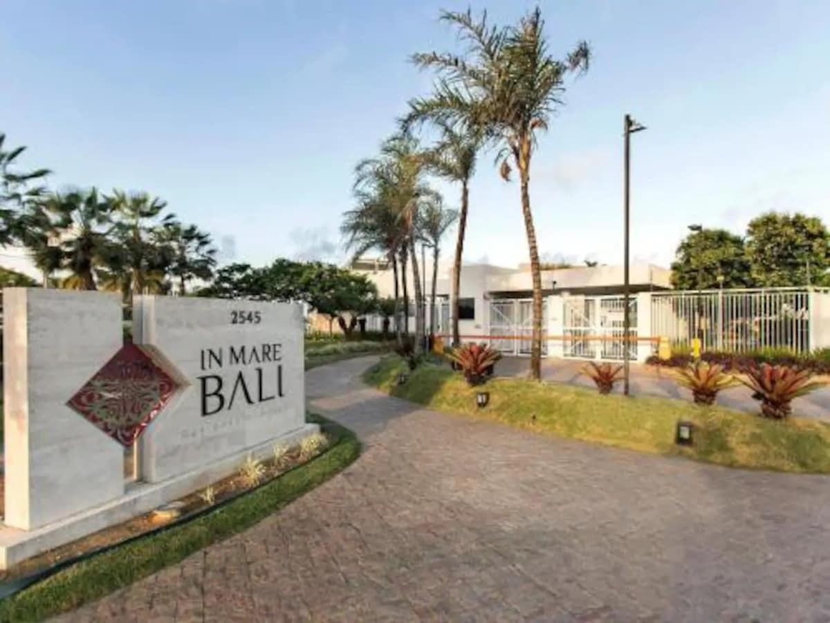 The entrance to the In Mare Bali Residential Resort is marked by a welcoming sign and lush palm trees. A well-maintained pathway leads to the property, surrounded by colorful tropical plants and gently landscaped areas. The atmosphere is calm and inviting, setting the tone for a relaxing stay.