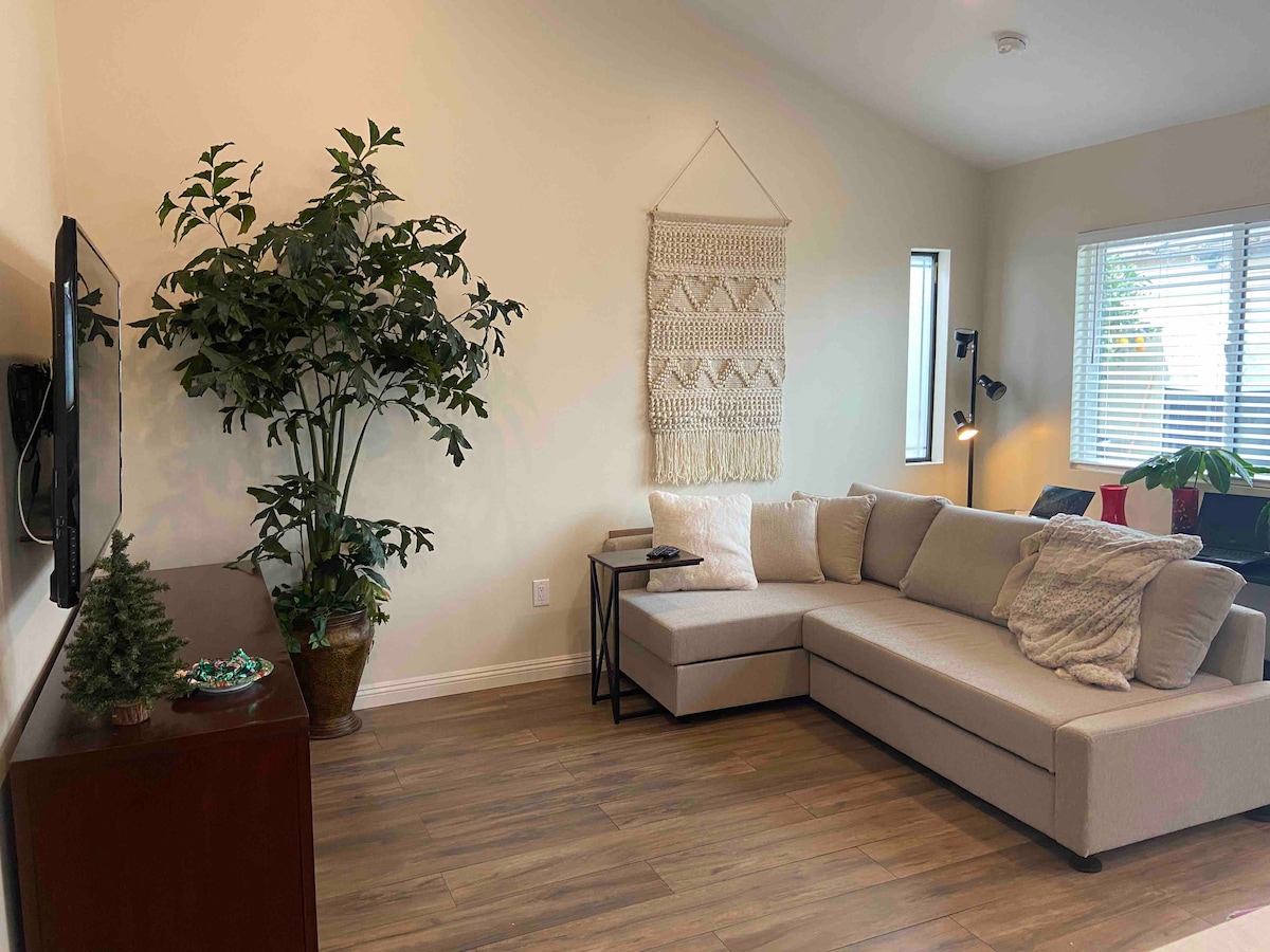 Sala de estar con sofá cama (que se muestra desde el área de la cocina). Área de trabajo con computadora portátil detrás del sofá.