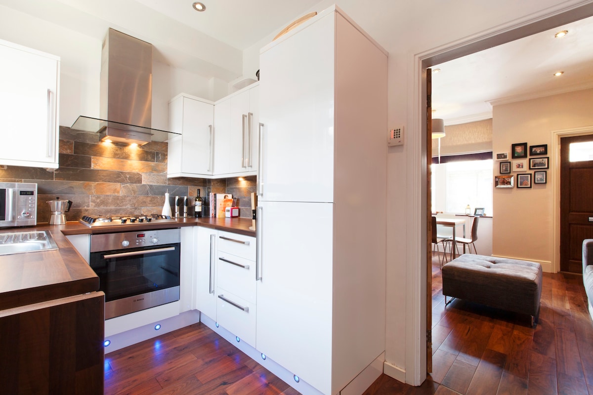 A modern kitchen is presented with white high gloss cabinetry and integrated appliances. A solid wood countertop contrasts with the cabinetry, while stone backsplash tiles provide texture. Soft lighting highlights the sleek design, creating a practical and inviting cooking space.