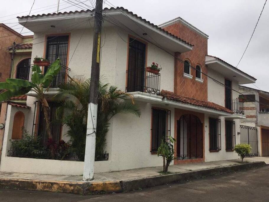 La casa está enmarcada con balcones floridos, jardineras y ventanales con toque colonial