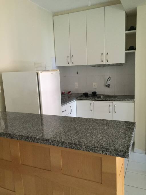 Cozinha estilo Americana, fogão elétrico, geladeira e louças em geral.