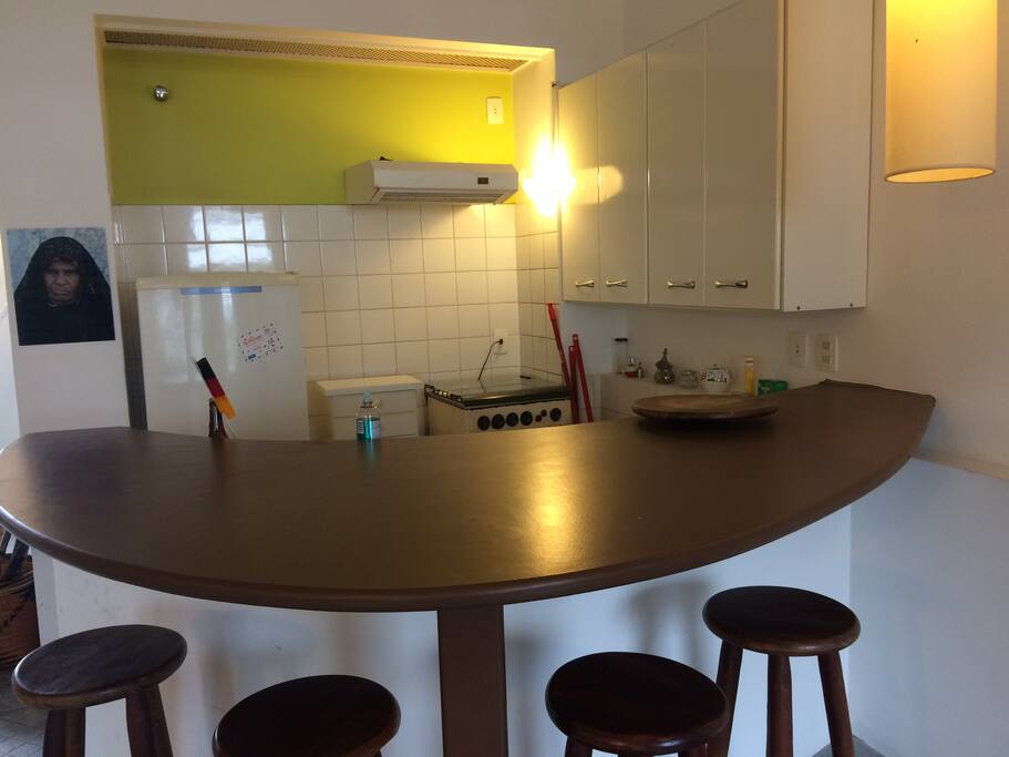 Cozinha americana com bancada, pia, fogão, geladeira, e todos os utensílios necessários para cozinhar.