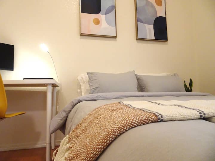 Kitanda chenye ustarehe na cha kisasa cha malkia kilicho na mashuka ya pamba ya hali ya juu. Karibu na kitanda kuna kituo cha kazi cha urefu unaoweza kubadilishwa na skrini ya inchi 30. 