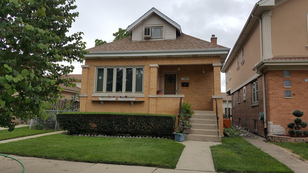 A well-built two-story brick home features a welcoming entry with a set of stairs leading to a front porch. Large windows allow natural light to enter, while neatly trimmed hedges and a landscaped area enhance the outdoor space.