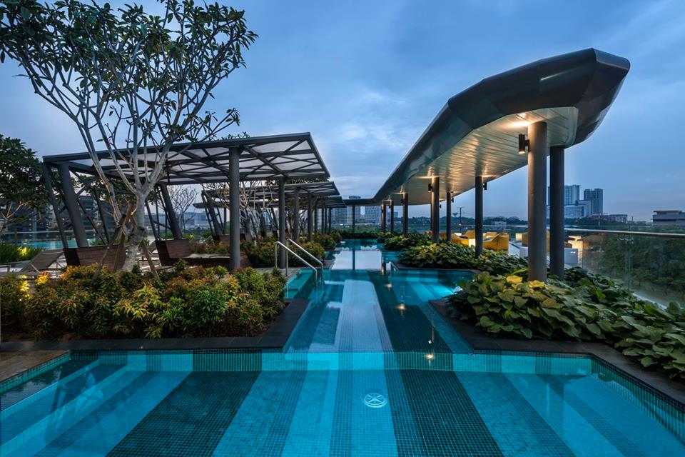 A rooftop pool area is highlighted, surrounded by lush greenery and modern seating. The tranquil water reflects the evening sky, while sleek umbrellas provide shade. The serene atmosphere invites relaxation with views of the city skyline in the background.