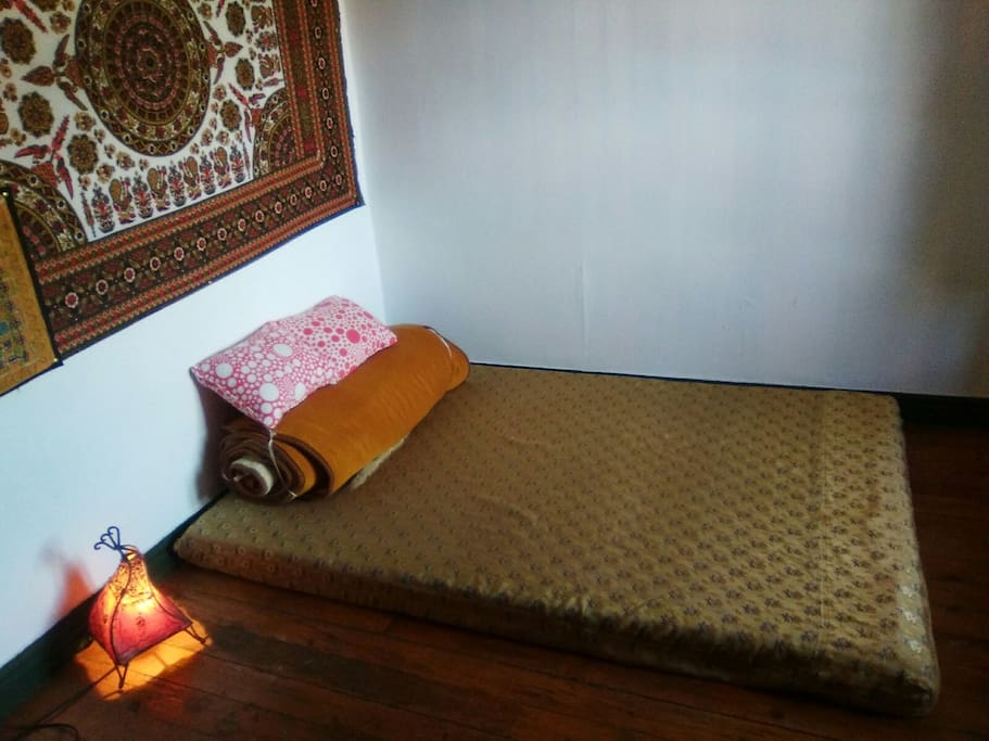 Cama doble estilo thai (sin somier) en habitación luminosa. La habitación tiene un pequeño escritorio.