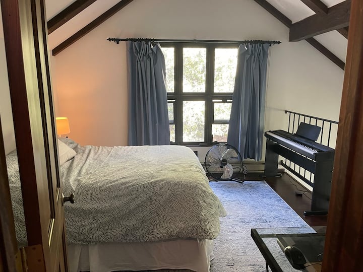 Лофт спалня с пълно легло, стъклено бюро и пиано.