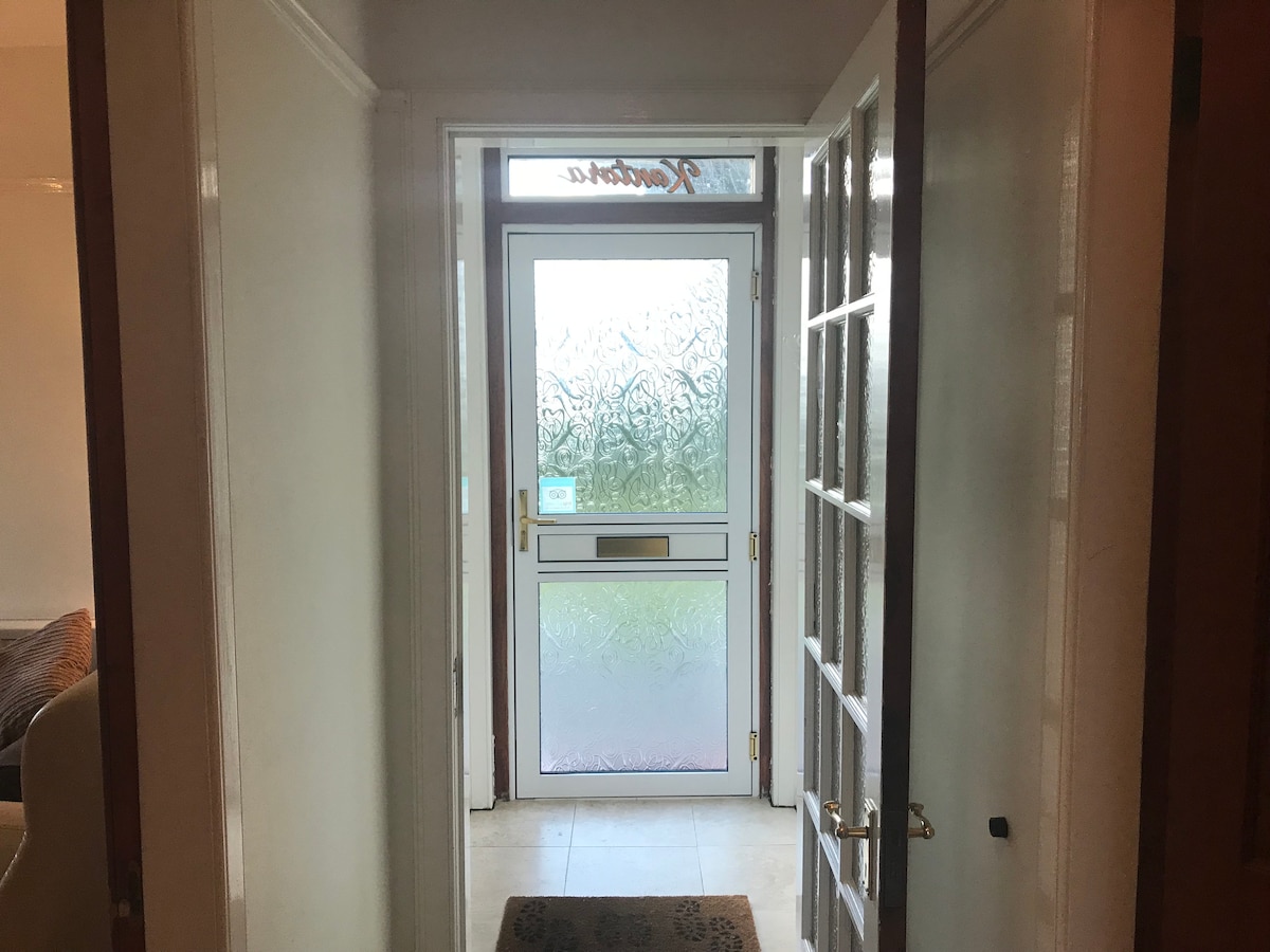 A welcoming entrance hallway is captured, featuring a clear glass panel door with decorative patterns. The space is illuminated by natural light, highlighting the tiled floor and a textured doormat. Open doors on either side lead into intimate living spaces.