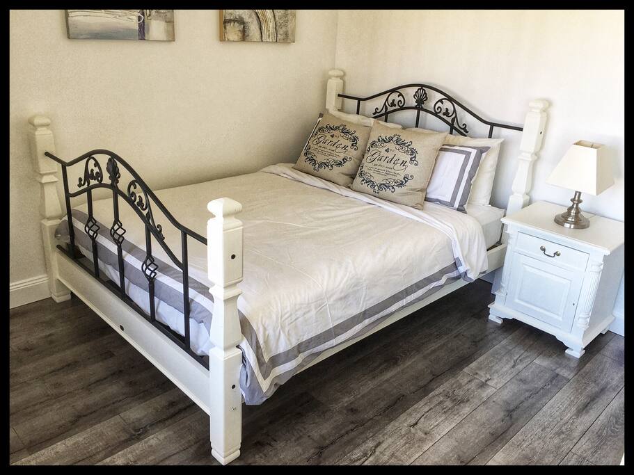 Queen size bed in a light airy room with bedside table, lamp and mirrored double wardrobe.
