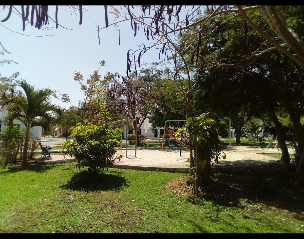 A neighborhood park is visible, featuring playground equipment surrounded by well-maintained greenery. Trees provide shade, and grassy areas invite relaxation. The playground includes swings and slides, creating a family-friendly atmosphere in this tranquil residential environment.