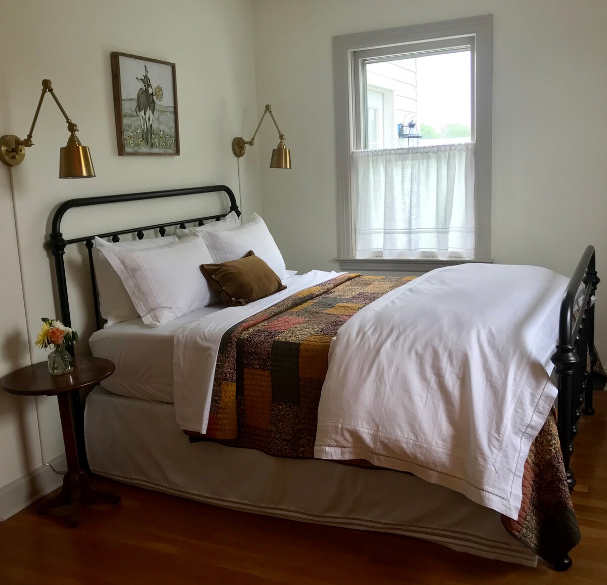 ห้องนอนชั้นหลักพร้อมเตียงเหล็กขนาดควีนไซส์ผ้าปูที่นอนสีขาวที่คมชัดและผ้าห่มเย็บปะติดปะต่อกัน