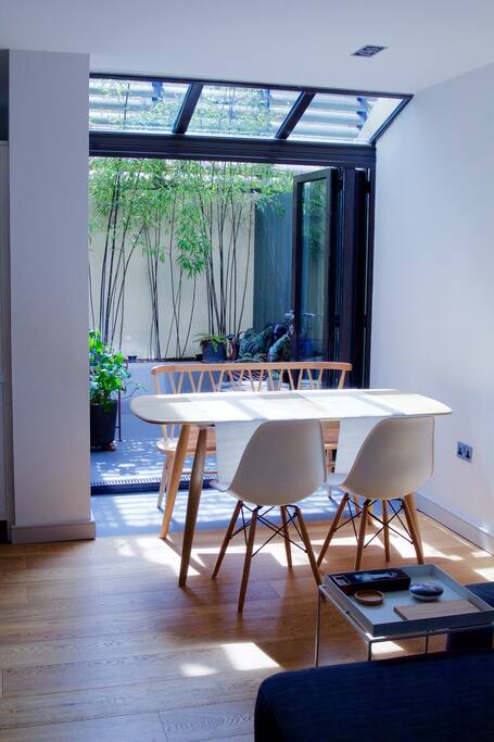 The light-filled dining area with Ercol dining table and mid-century chairs. There are bi-folding doors that open onto the sunny private courtyard
