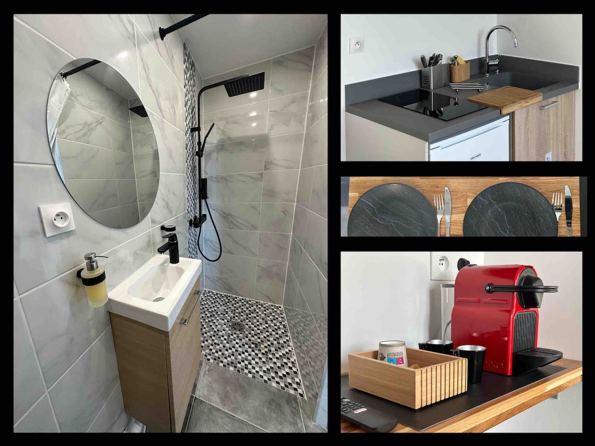 A modern bathroom is showcased, featuring a stylish circular mirror above a compact sink. A glass shower with a rainfall showerhead is set against tiled walls. In another section, a kitchenette includes a countertop with a sink and cooking area, alongside a coffee machine and neatly arranged dining accessories.