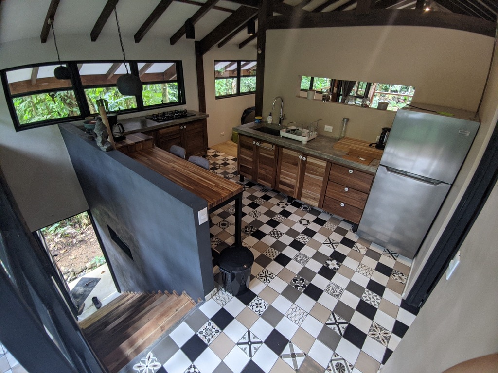The kitchen showcases wood cabinetry and modern appliances, including a stainless steel refrigerator. A large countertop provides ample workspace, while patterned tiles create a unique flooring design. Natural light enters through several windows, enhancing the inviting and functional atmosphere.