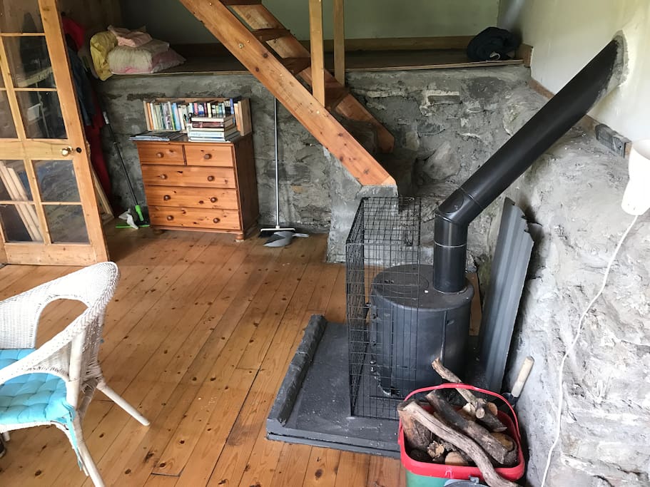 Downstairs living area - wooden floors and wooden stair case with stone walls and woodburner.