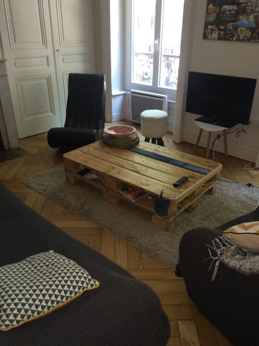 Espace salon avec un canapé dépliant en lit 2 places, avec son parquet atypique, ses grandes fenêtres et sa cheminée