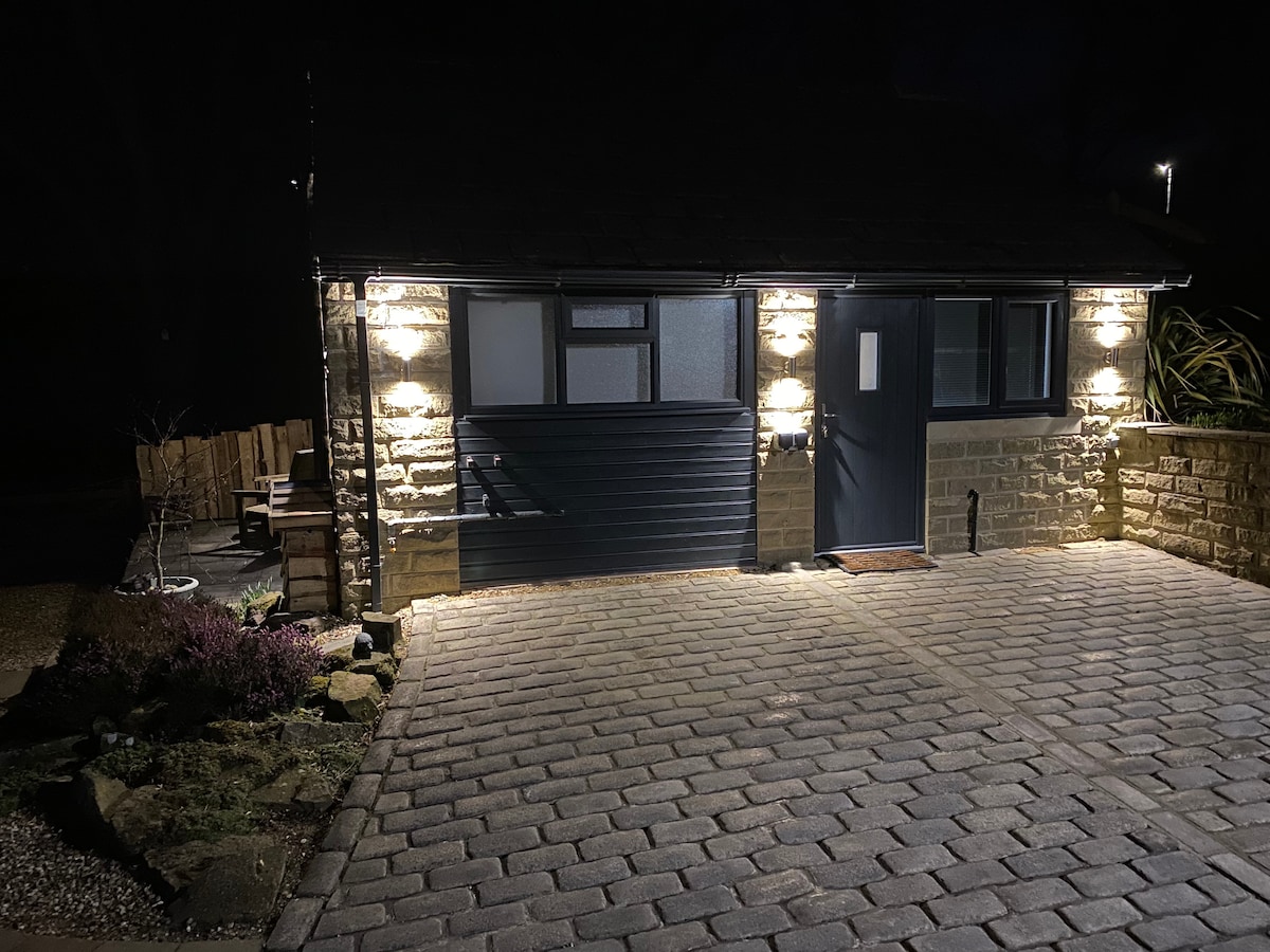 The exterior of Water's Edge is captured at night, showcasing the stone-clad wall and well-lit entrance. A pathway of cobblestones leads to the door, while outdoor seating is visible to the left, providing a cozy outdoor gathering space.