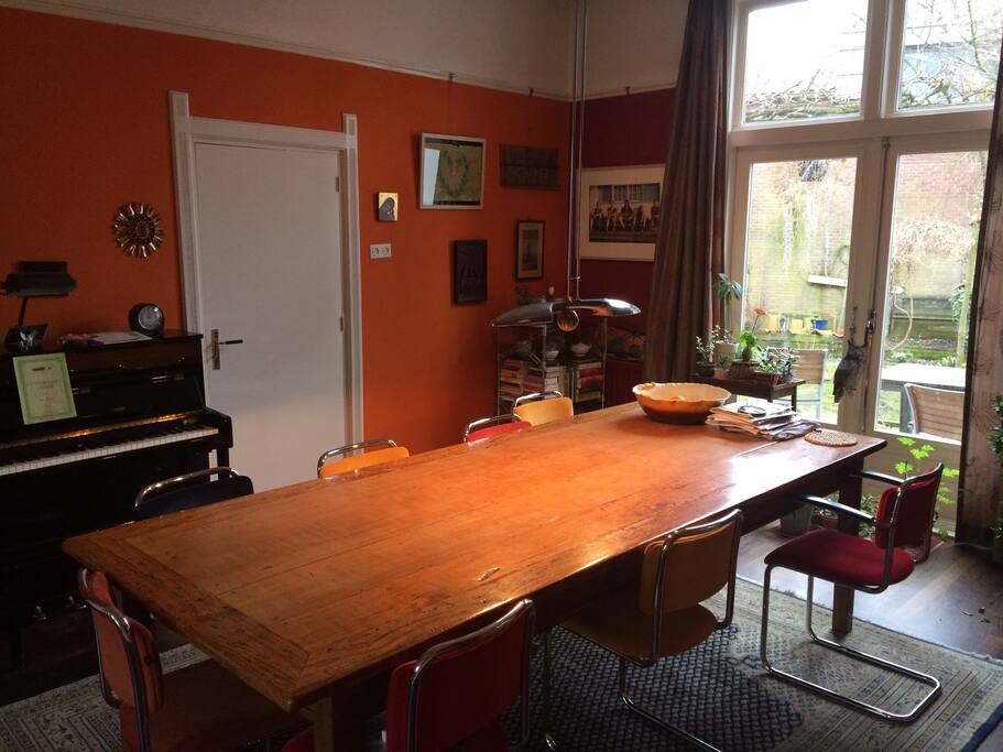 Living room with big wooden table, piano and doors to garden