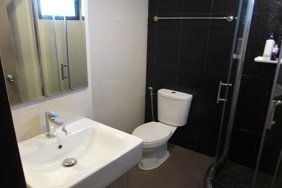 A modern bathroom features a walk-in shower with glass doors and a handheld showerhead. A sleek white sink sits beside a large mirror, with a toilet positioned nearby. The space is accented by contrasting black and white tiled walls.