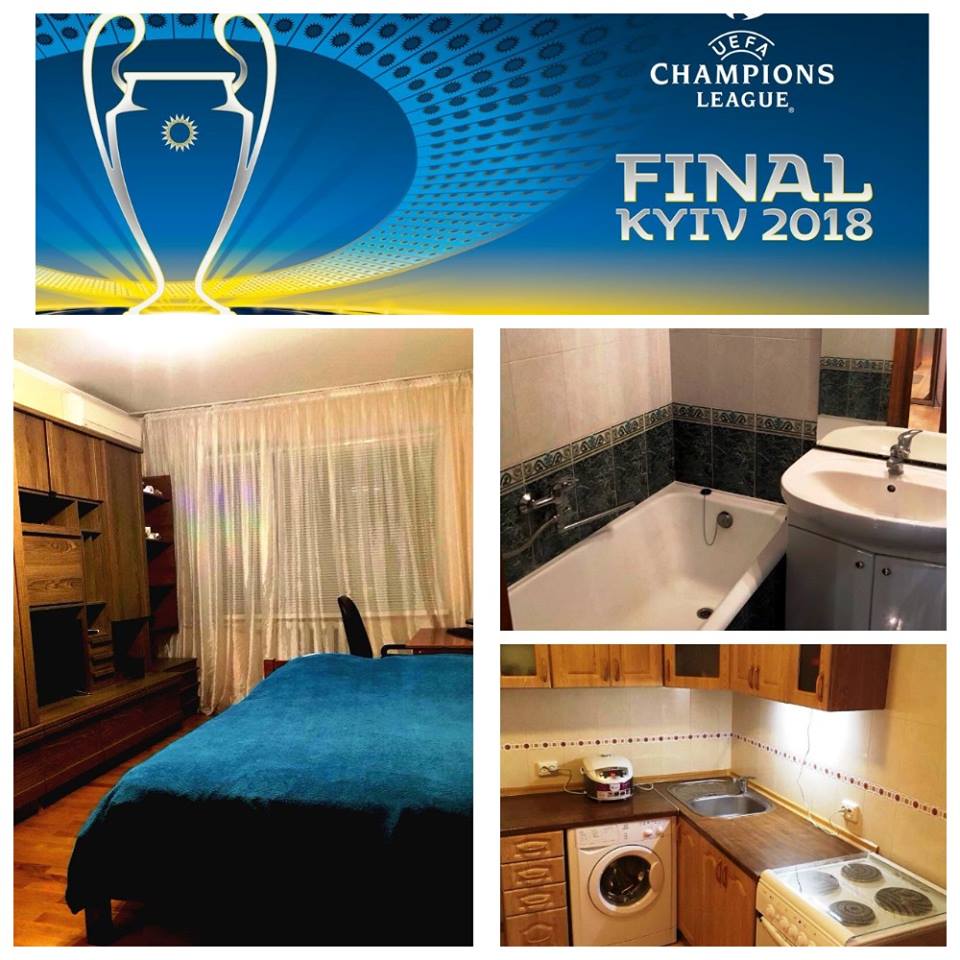 The image displays a cozy bedroom featuring a spacious bed with a dark blue bedspread and a wooden wardrobe. A bathroom area is visible, showcasing a bathtub and a sink. The kitchen corner includes modern appliances, including a washing machine and an electric kettle.