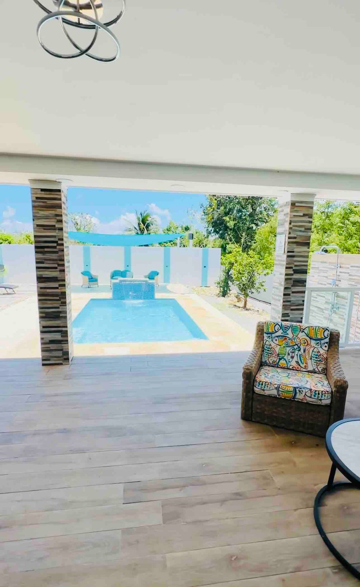 A private pool is visible through expansive sliding glass doors, allowing natural light to fill the space. A comfortable chair with a colorful cushion is positioned nearby, creating a relaxed outdoor lounging area. Lush greenery surrounds the pool, providing a serene atmosphere.