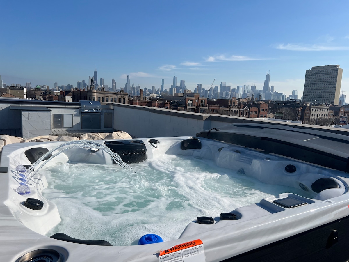 A rooftop hot tub is showcased against a panoramic view of the Chicago skyline. The tub features jets and a spacious seating area. Clear blue skies and distant city buildings enhance the relaxing atmosphere, inviting guests to unwind while enjoying the urban scenery.