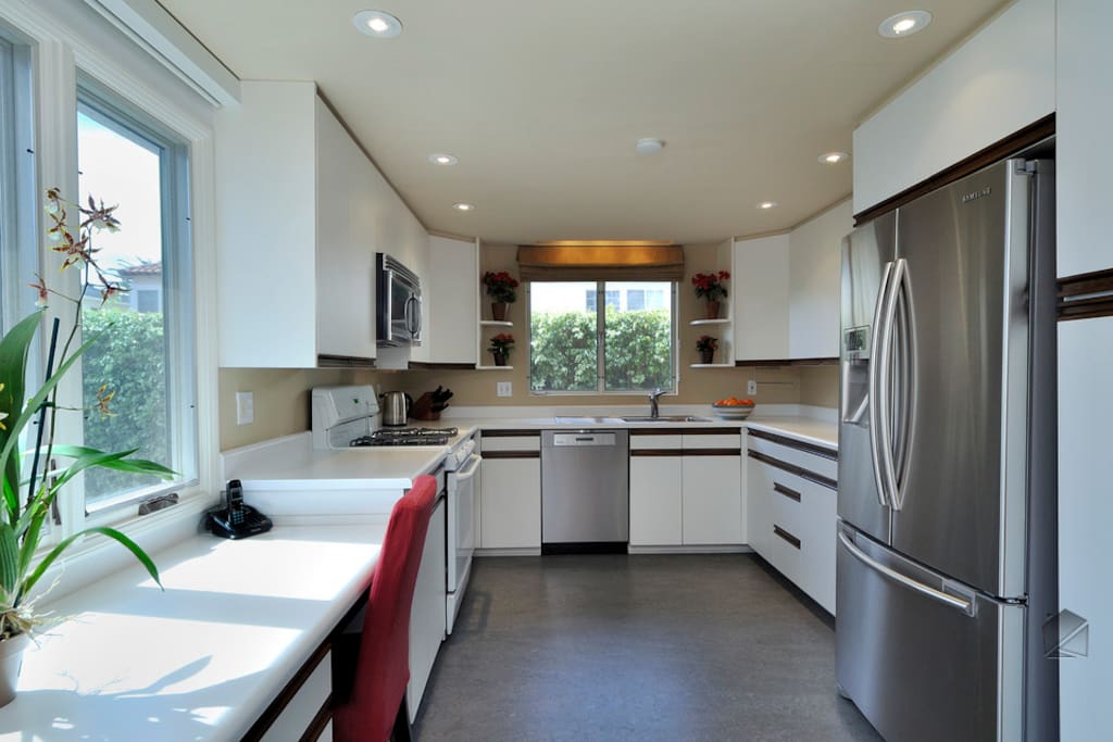 The sleek, modern kitchen has a Samsung stainless steel refrigerator, Miele dishwasher, microwave, built-in desk, and gas stove and oven.