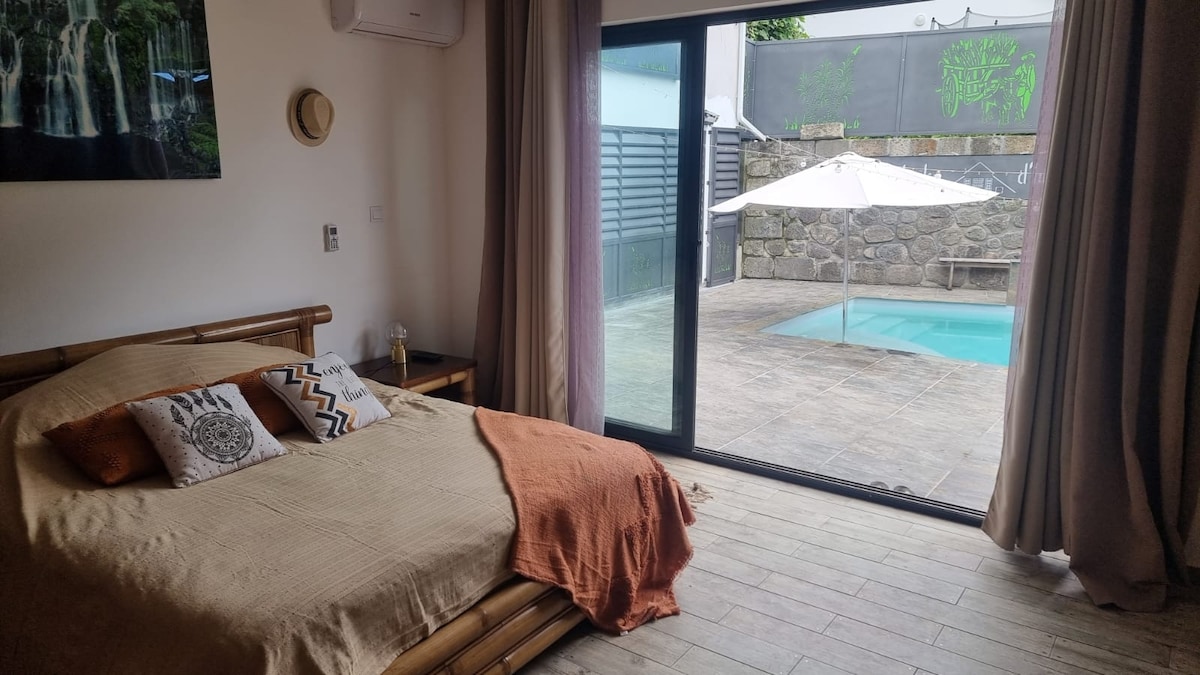 A spacious bedroom features a queen size bed adorned with decorative pillows and a soft throw. Large glass doors provide direct access to the pool area, allowing natural light to enter. A relaxing atmosphere is complemented by neutral decor and wood accents.
