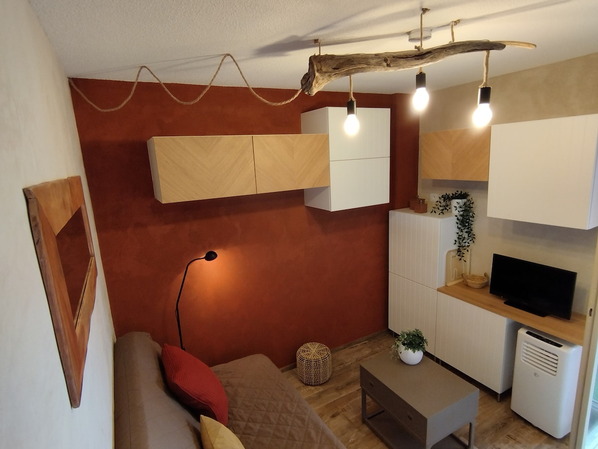 A cozy living area is presented, featuring a textured brown wall and light-colored cabinetry. The space includes a sofa, a coffee table, and a television unit. Ambient lighting is provided by pendant lights suspended from the ceiling, complemented by a decorative piece on the wall.