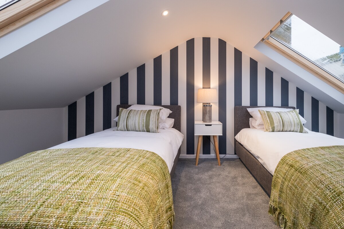 Elegante dormitorio tipo loft gris, dos camas individuales, inodoro privado.