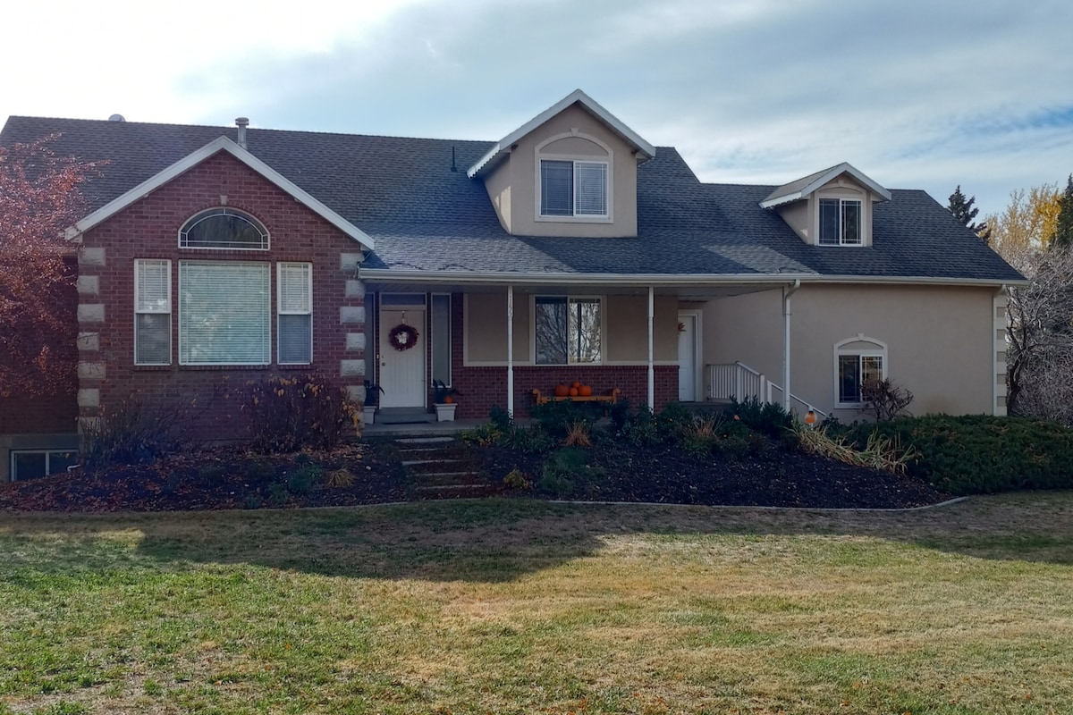 A spacious house is showcased with a brick facade and light-colored upper sections. Large windows allow for plenty of natural light, while neatly arranged flower beds and lawn add to the home's appeal. The welcoming entrance features steps leading to a covered porch.