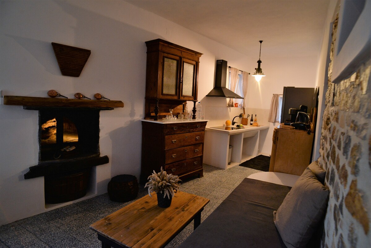 A welcoming living area is highlighted by a wooden coffee table and a comfortable sofa. An elegant sideboard adds charm, while an open kitchen area includes a stove and modern appliances. Natural light pours in through a window, enhancing the cozy ambiance.