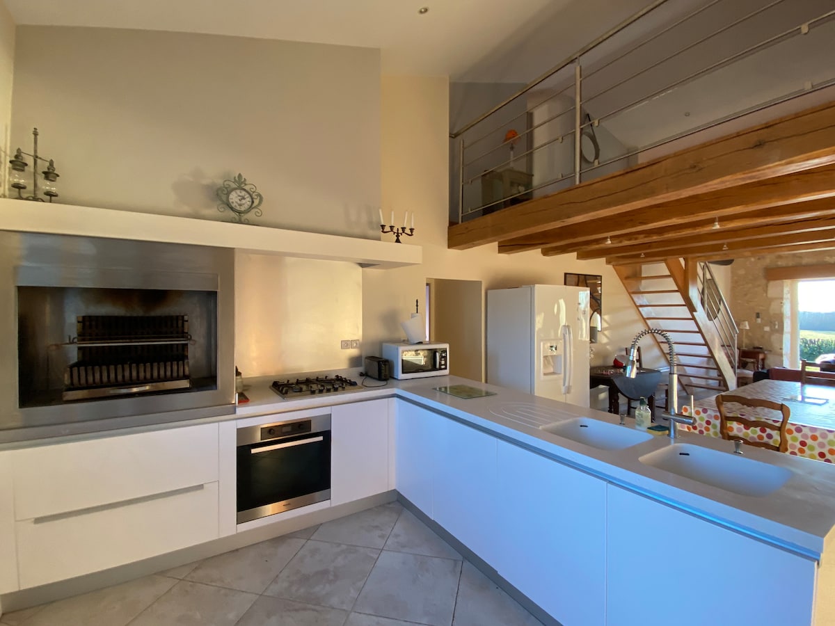 An open kitchen area showcases modern appliances, including an oven and microwave. A spacious countertop offers ample workspace, while a staircase leads to an upper level. Natural light fills the room through a window, creating a bright and functional cooking environment.