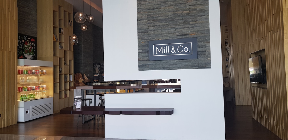 An inviting lobby area features a sleek reception desk with a stone backdrop. Above, modern pendant lights hang gracefully, casting a gentle glow. A beverage display showcases a variety of colorful drinks, while wooden accents add warmth to the contemporary design.