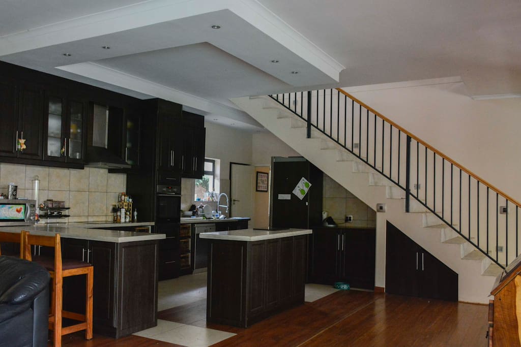 Open plan kitchen with stairs leading to 5 bedrooms upstairs and additional reception area with TV
