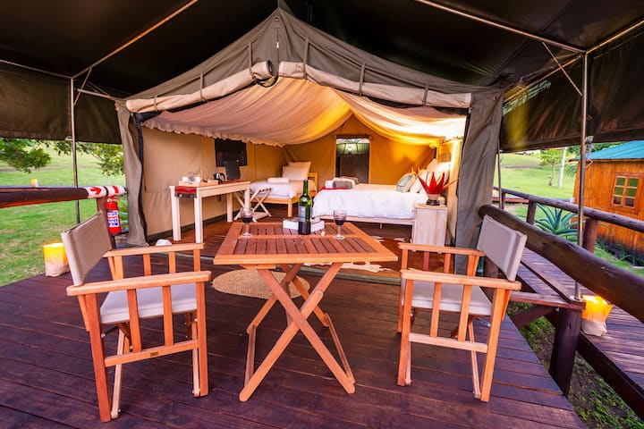 A spacious 2 roomed glamping tent with a comfortable queen size bed and 2 singles, with its own patio and seating area overlooking the lake and lush green gardens. Leads onto a double vanity and outdoors to a semi enclosed open air shower.