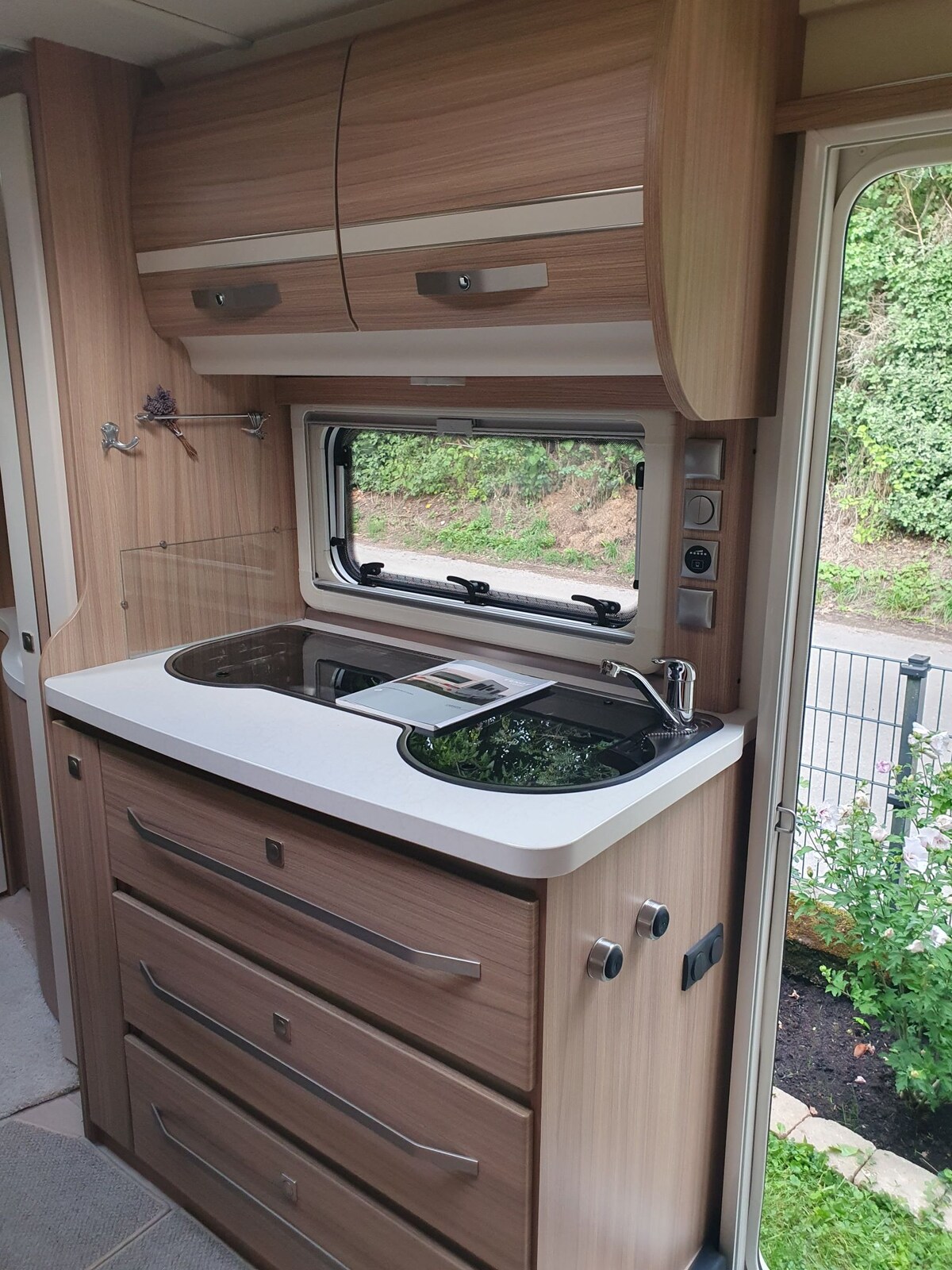 A compact kitchen area features wooden cabinetry and a countertop with a sink and cooking space. Storage drawers below provide functionality, while a window allows natural light and views of the surroundings. The modern design emphasizes practicality in a cozy living space.