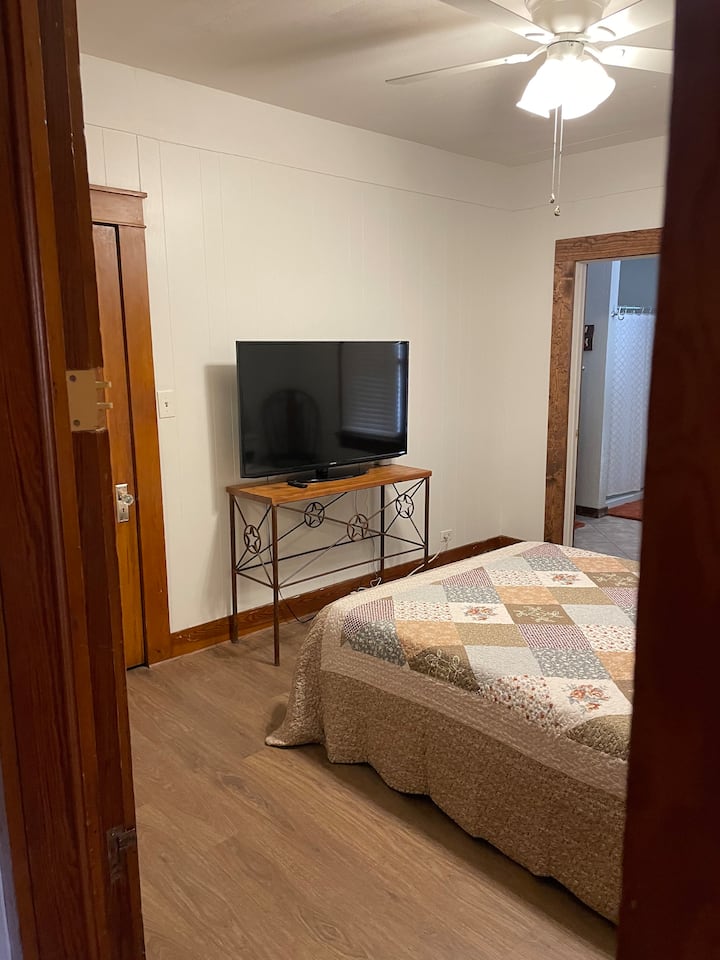 Földszinti hálószoba queen méretű ággyal , TV-vel és csatlakozó fürdőszobával.