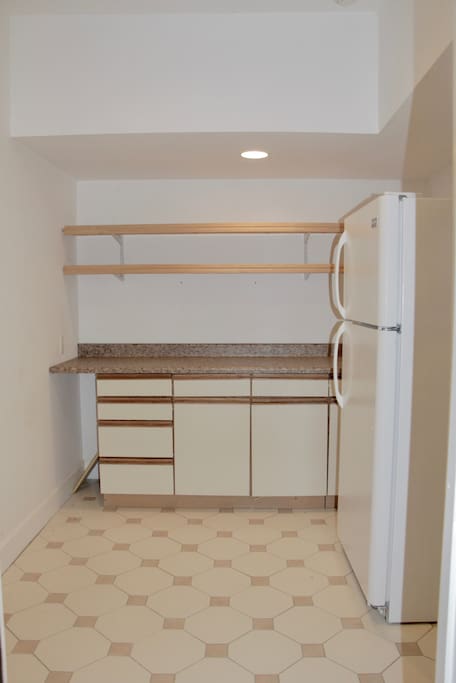 Kitchen area with a microwave , refrigerator , coffee maker . Glasses , cups and dishes .