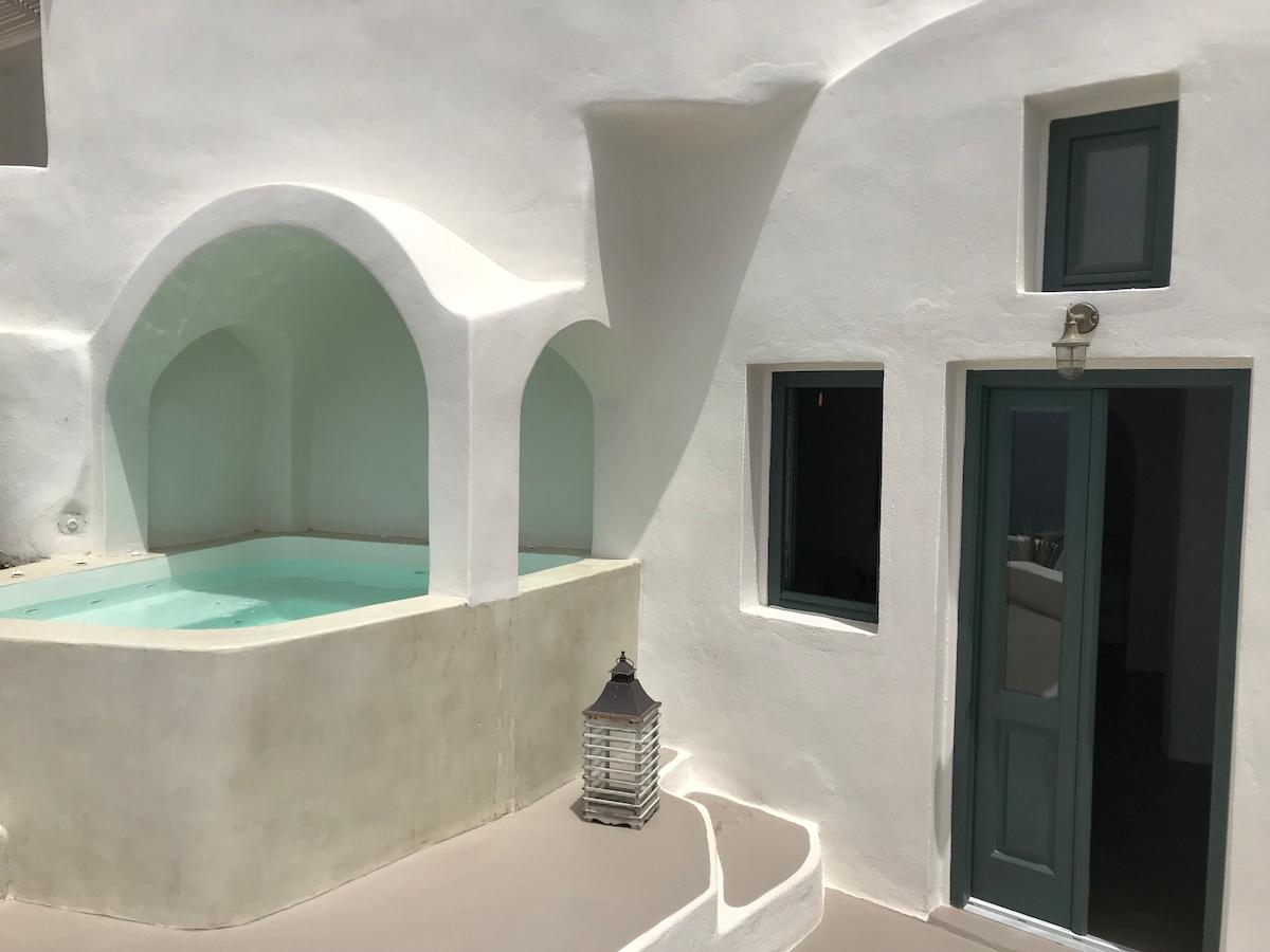 A private outdoor plunge pool is set against a backdrop of smooth white walls, featuring rounded architectural elements. A door with a blue frame leads into the accommodation, complemented by a small lantern positioned on the pool deck, providing a serene atmosphere.