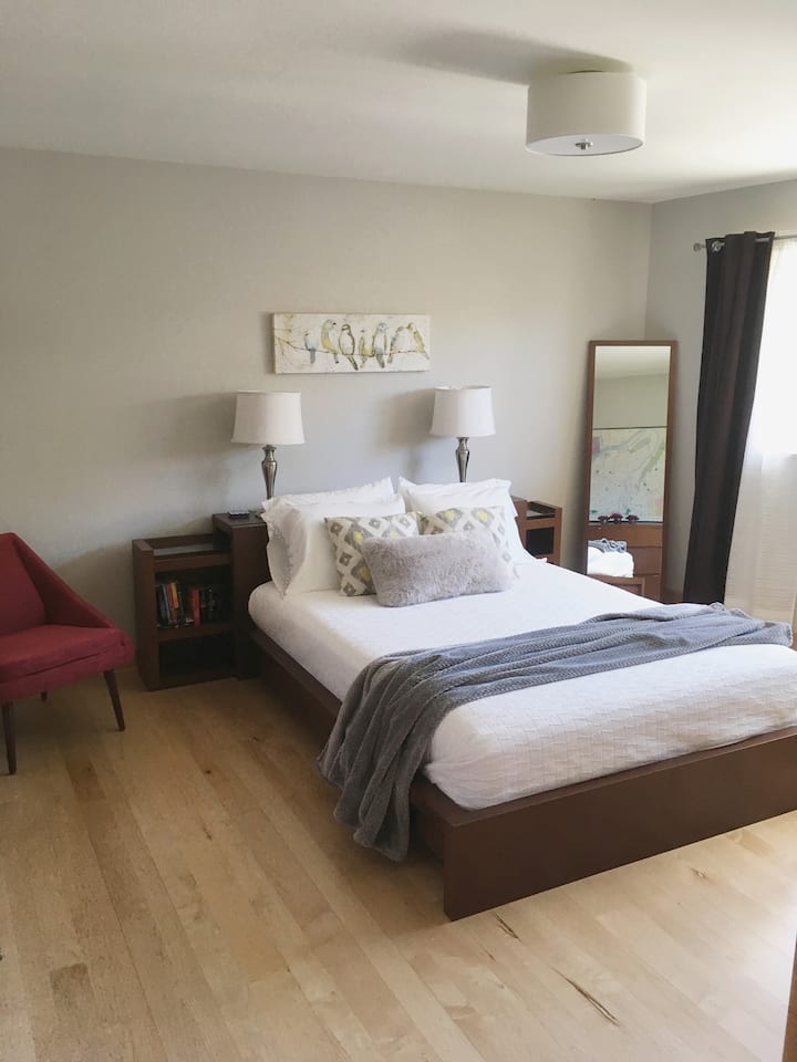 Otra vista del dormitorio con la cama de espuma viscoelástica de tamaño queen y silla de estar.  Hay cortinas opacas para una gran noche de descanso.
