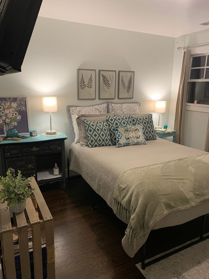 ห้องนอนใหญ่ด้านหลังบ้านพร้อมเตียงขนาดควีนไซส์ที่สะดวกสบายที่ประกอบด้วยที่นอนเด็กแบบปรับได้ผ้าปูที่นอนผ้าฝ้ายออร์แกนิกทีวีแบบสตรีมมิ่งแบบติดผนังและประตูทางออกไปยังลาน/ระเบียงด้านหลัง